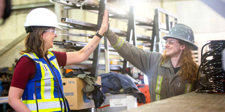 Premier Danielle Smith in a hard hat high-fiving a worker in a shop