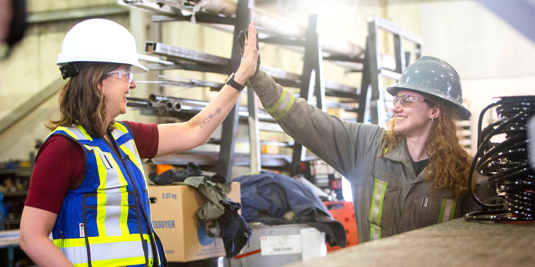 Premier Danielle Smith in a hard hat high-fiving a worker in a shop