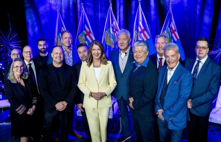Danielle Smith on stage with a group in front of Alberta flags