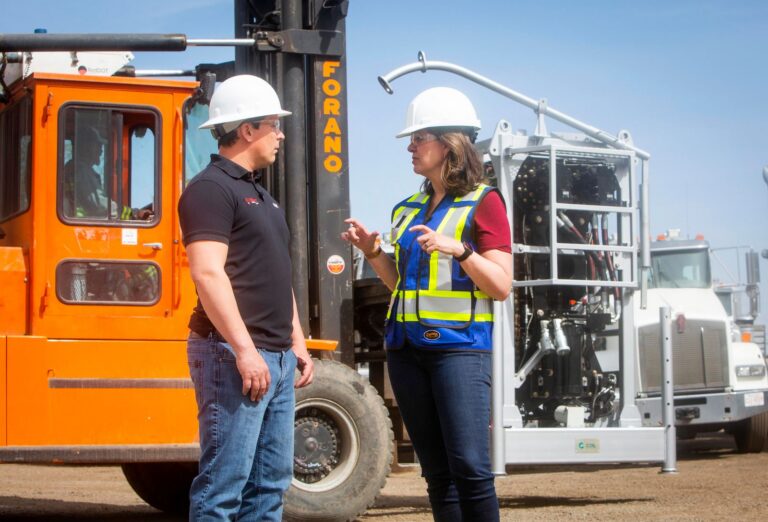 Danielle Smith in a hard hat talking with a worker beside a forklift
