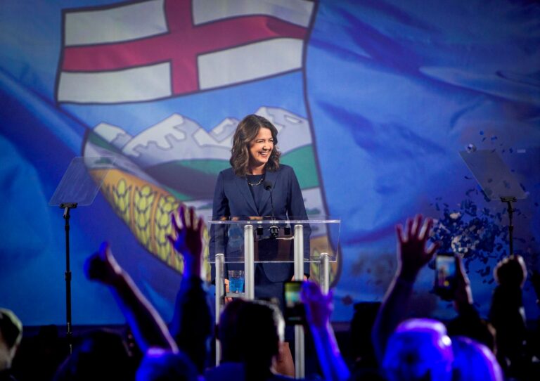 Danielle Smith at the podium in front of an Alberta flag as supporters cheer